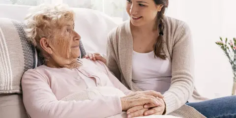 Młoda kobieta wspiera starszą panią, która może potrzebować pomocy w leczeniu alzheimera. Ich dłonie splecione są w geście troski.