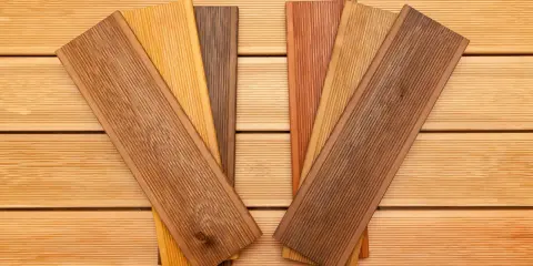 Verschiedene Holzproben mit unterschiedlichen Farben und Maserungen liegen auf einer Holzoberfläche. Sie zeigen die Vielfalt der dauerhaftigkeitsklassen holz für Terrassendielen.