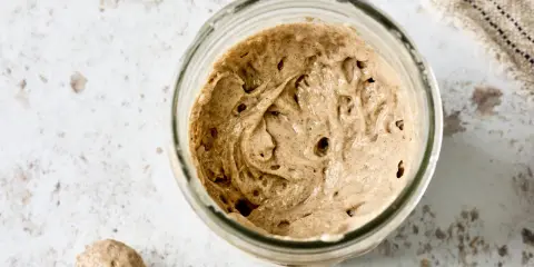 Ein Glas mit Sauerteig, angesetzt mit Roggenvollkornmehl, zeigt Bläschen und eine lebendige Textur.