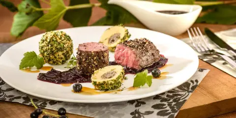 Edles Fleischgericht mit Johannisbeeren verwerten: zartes Rinderfilet, umhüllt von Kräutern und Nüssen, serviert mit einer fruchtigen Johannisbeersauce und Beilagen.