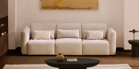 Sofá beige con cojines, mesa de centro oscura, alfombra clara y cuadro abstracto. Los colores feng shui crean un ambiente sereno.