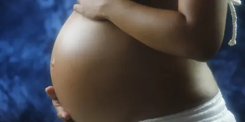 Pancia di donna incinta, con mani che la accarezzano. Si intravede un bikini bianco e uno sfondo blu. L'addome è tonico, forse con un leggero intestino iperecogeno visibile.