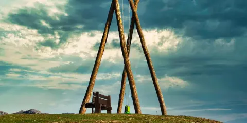 Un columpio ríachuelo solitario en la cima de una colina, con un banco y una mochila verde, bajo un cielo dramático.