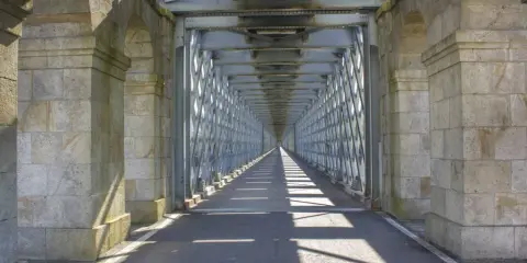 El **puente internacional Tui** se alza imponente, un túnel de metal y piedra que se pierde en la distancia, proyectando sombras geométricas sobre el asfalto.