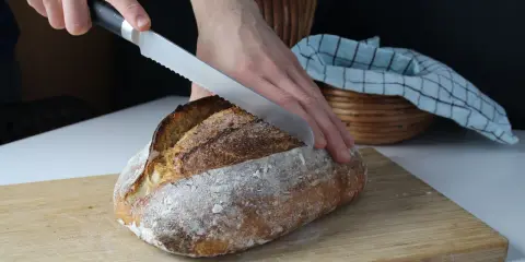 Krojony bochenek chleba z długim terminem ważności, z chrupiącą skórką, na desce do krojenia.