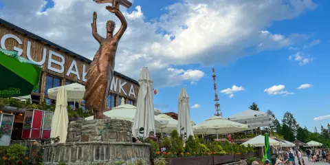 Gubałówka atrakcje: pomnik z orłem, restauracje, parasole i ludzie odpoczywający na ławkach.