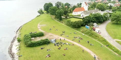 En grupp människor njuter av en paus under sin vandring i Danmark. En kyrka med tegeltak syns i bakgrunden.