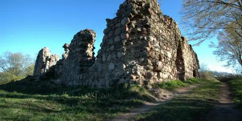 Kamienne ruiny zamku w Kurzętniku, porośnięte trawą, stoją na wzgórzu pod błękitnym niebem.
