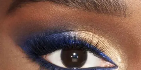 Ojo con un audaz maquillaje de ojos azul y dorado. Delineador azul vibrante y sombras doradas brillantes resaltan la mirada.