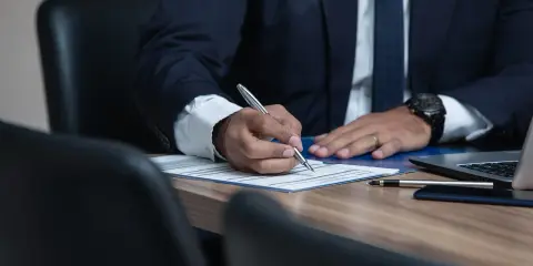 Prawnik w garniturze podpisuje dokumenty przy biurku.