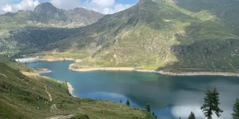 Sentiero facile tra i laghi gemelli alpini, con montagne verdi e un cielo azzurro con nuvole bianche.