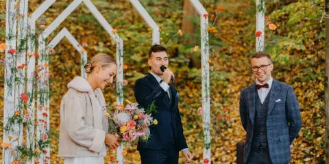 Piękna panna młoda z bukietem, pan młody przemawia do mikrofonu, a pan młody z uśmiechem. Wesele jesienią w otoczeniu kolorowych liści.