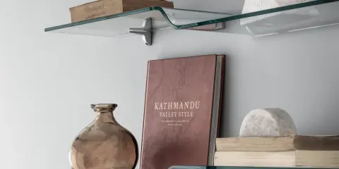Idee mensole ingresso: vetro curvo con libri antichi, vaso ambrato e scultura in marmo.
