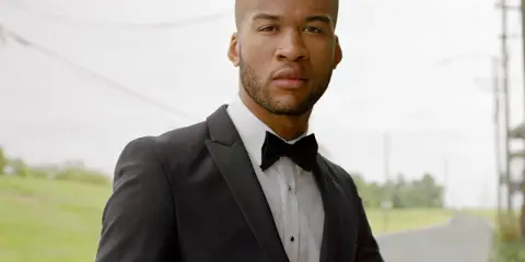 A man in a black tuxedo with a bow tie, ready for black tie weddings.