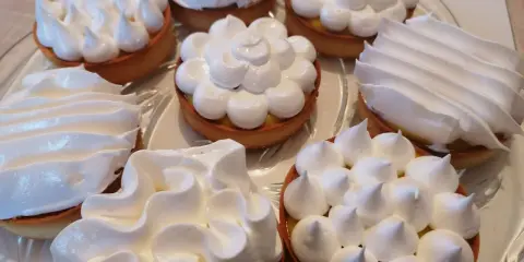 Assortiment de tartelettes garnies d'une crème citron et surmontées de **meringue italienne** aux formes variées.