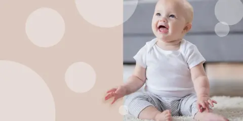 Uśmiechnięte dziecko siedzi na dywanie. Czy 5 miesięczne dziecko można sadzać na kolanach?