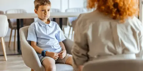 Chłopiec siedzi zmartwiony, rozmawiając z terapeutką. Czy sąd może zmusić dziecko do kontaktów z ojcem?