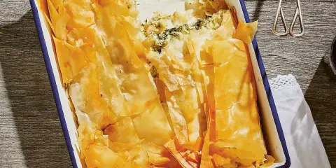 En gyllene, krispig spenatpaj i en blå kantad form. Perfekt för ett spanakopita recept.