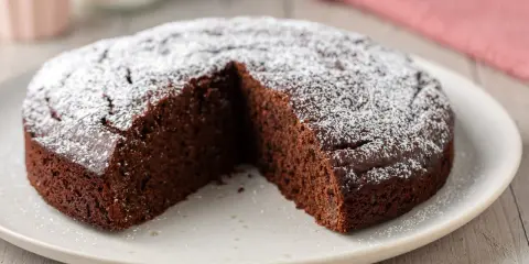 Una fetta è stata tolta da una torta al cioccolato morbida, cosparsa di zucchero a velo.
