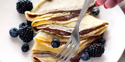 Piatto di crepes alla Nutella, guarnite con mirtilli e more, pronte per essere gustate.