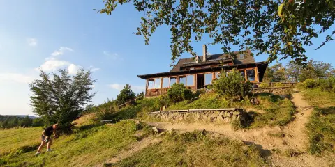 Bacówka PTTK nad Wierchomlą, drewniany dom z werandą, otoczony zielenią, zaprasza turystów na górskie szlaki.