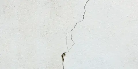 Una grieta fina y profunda recorre una pared blanca, mostrando diferentes tipos de grietas en techos y paredes.