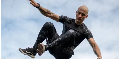 Mężczyzna w ruchu, jakby ćwiczył hiit. Co to za trening? Dynamiczne skoki i akrobacje na tle nieba.