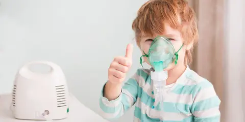 Chłopiec z gorączką i przyspieszonym oddechem używa nebulizatora, pokazując kciuk w górę.