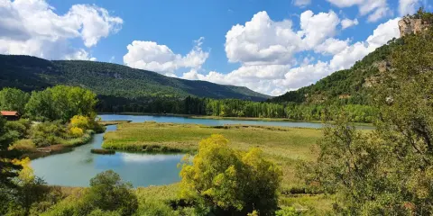 Paisaje de lagunas y montañas verdes, ideal para rutas senderismo Cuenca. Cielo azul con nubes blancas.