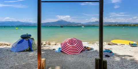 Słoneczne plaże nad jeziorem Garda, z parasolami, leżakami i wodnymi atrakcjami w tle.