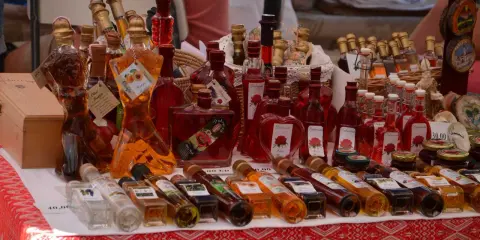 Różnorodne butelki z rakiją, w tym te w kształcie kobiecym, oferowane na targu. Co to rakija? To tradycyjny alkohol, często owocowy.