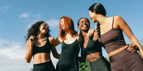 Quatre femmes souriantes, en tenue de sport, profitent du soleil. Leurs abdos sont visibles, suggérant une pratique comme l'abdo hypopressif.