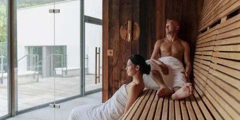 Para dowiedzieć się, jak korzystać z sauny w hotelu, relaksuje się w drewnianej saunie z widokiem na nowoczesny basen.