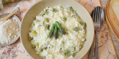 Kremowe risotto ze szparagami, posypane parmezanem, z kilkoma zielonymi szparagami na wierzchu.
