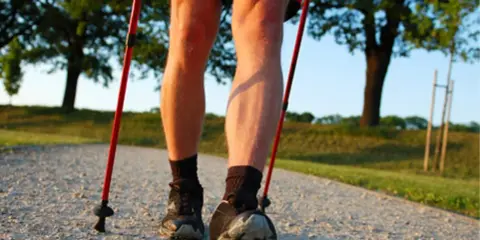 Nogi w butach do nordic walking, z kijkami w rękach, na ścieżce. Dowiedz się, jak prawidłowo założyć buciki na kijki nordic walking.