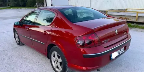 Błyszczący czerwony Peugeot 407 2.0 HDI z przyciemnianymi szybami stoi na żwirowym podjeździe.