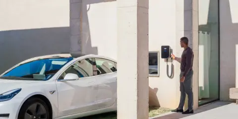 Uomo accanto a un'auto elettrica bianca, che interagisce con una wallbox V2C. Un bonus per la ricarica intelligente.