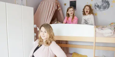 Wesołe dziewczynki w łóżku piętrowym w pokoju dla rodzeństwa. Mama uśmiecha się obok.