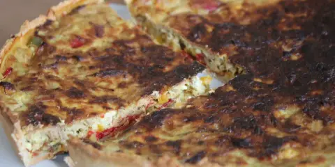 Une part de quiche poivron feta dorée, avec des morceaux de poivrons colorés et de feta crémeuse dans sa garniture.
