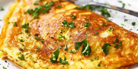 En gyllene omelett, perfekt för ett snabbt omelett recept, toppad med färsk persilja och en nypa salt.