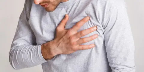 Mężczyzna trzyma rękę na piersi, odczuwając dziwne zatykanie w klatce piersiowej.