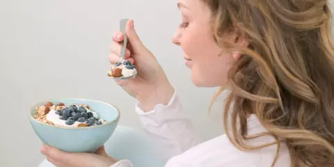 En kvinna äter en skål med yoghurt, blåbär och nötter. En hälsosam frukost som kan hjälpa till att få ner blodsockret.