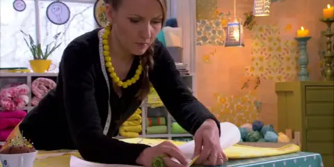 Kvinna med gult halsband mäter tyg för att sy topp.
