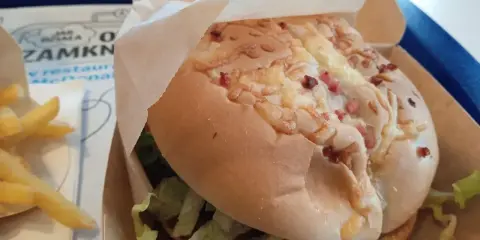 Pyszny burger drwala z chrupiącym bekonem i serem, w papierowym opakowaniu, obok porcji frytek.