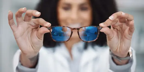 Kobieta w białym kitlu prezentuje okulary relaksacyjne z niebieskimi soczewkami, odbijającymi wnętrze sklepu.