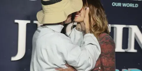 Justin Biebers fru, Hailey, ler när de kysser varandra framför en bakgrund med texten "Justin Bieber: Our World".