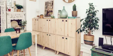 Muebles de madera clara con tiradores verdes, una mesa con sillas turquesas y una chimenea decorada. Inspiración para tu gama de colores para pintar muebles de madera.