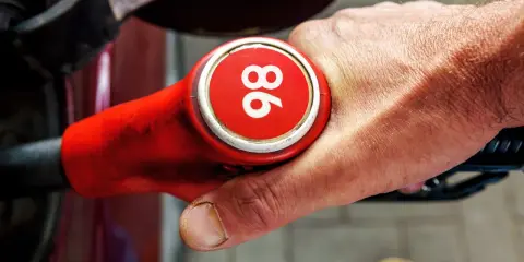 Mano sujetando una boquilla de gasolina roja con el número 96, indicando uno de los tipos de gasolina en España.