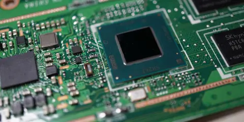 Zbliżenie na zieloną płytę główną z widocznymi częściami laptopa: procesorem, układami pamięci i innymi komponentami elektronicznymi.