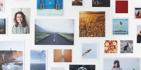 Un collage di fotografie su una parete bianca: paesaggi, ritratti, natura. Un'idea su come esporre fotografie in modo creativo.